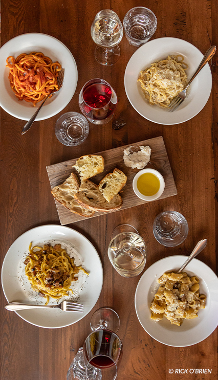 A wooden table set with fresh bread, pasta, and wine. Image copyright Rick O'Brien.